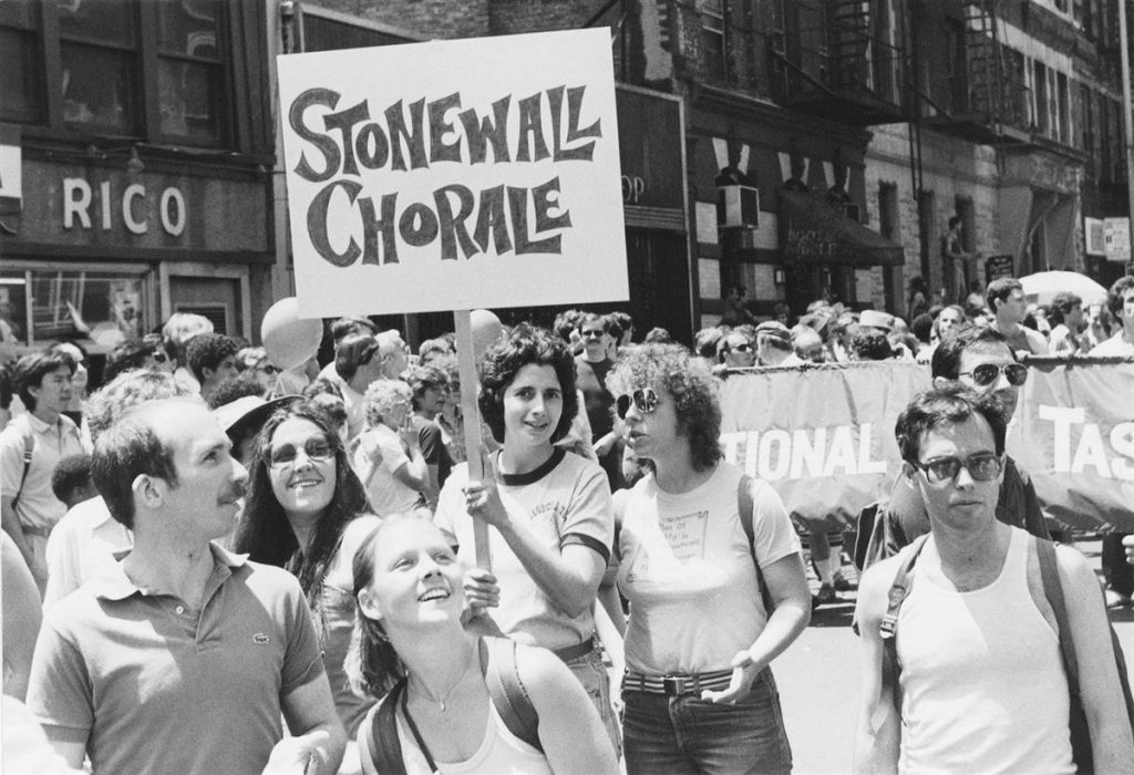 Photograph of parade goers at a NYC Pride parade with a sign that reads "Stonewall Choral."